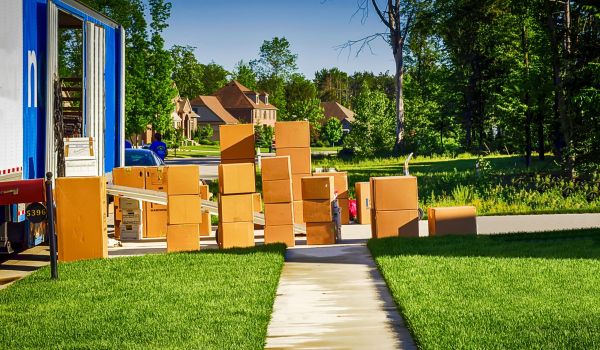 A few boxes in a yard, waiting to be moved into the house after a move. A nearly unloaded truck is parked nearby.