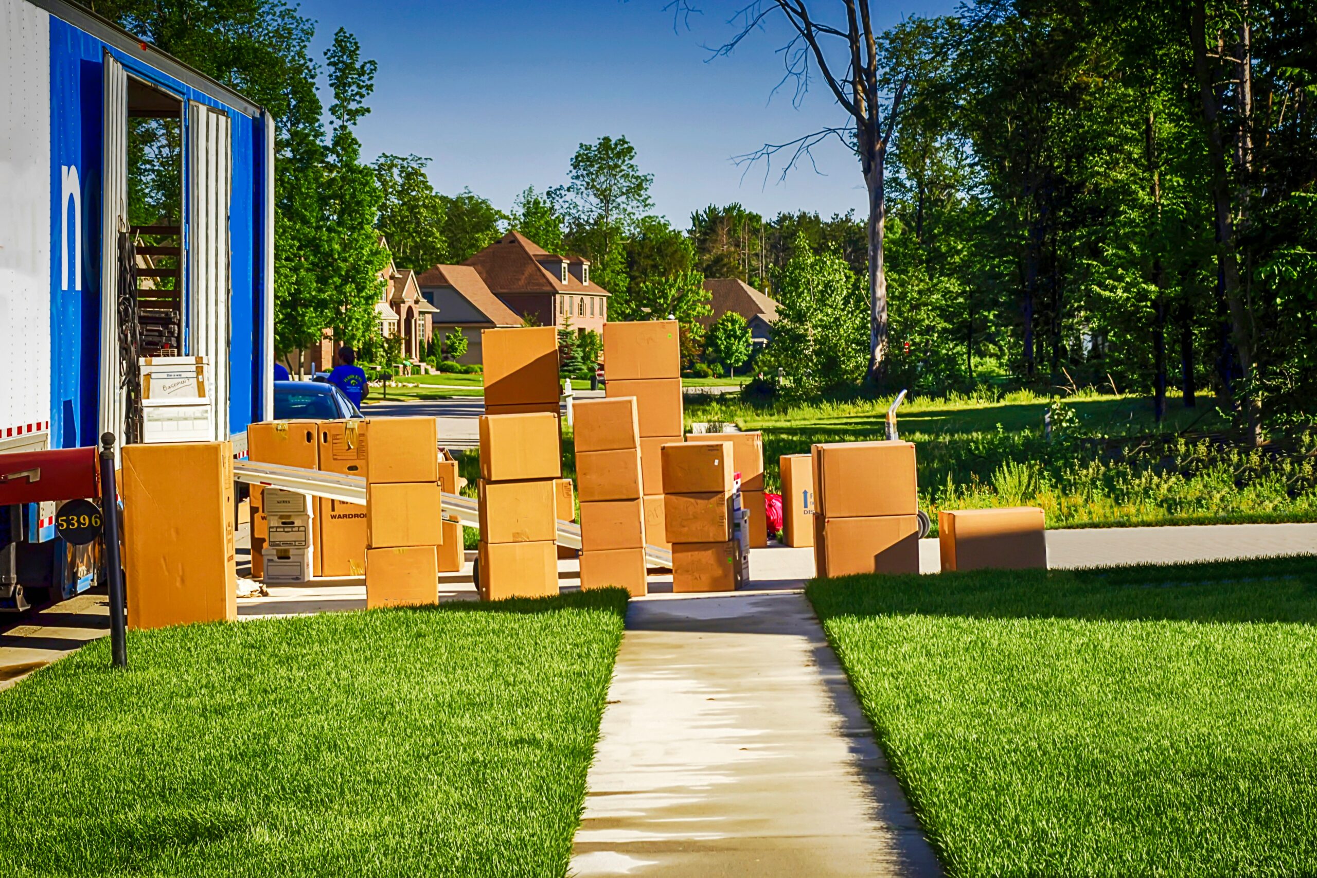 A few boxes in a yard, waiting to be moved into the house after a move. A nearly unloaded truck is parked nearby.