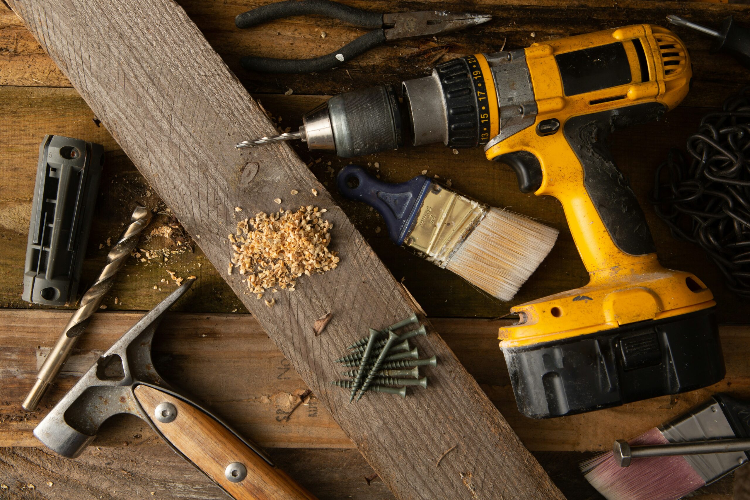 A few DIY tools on a table, with a piece of wood and some wood shavings.