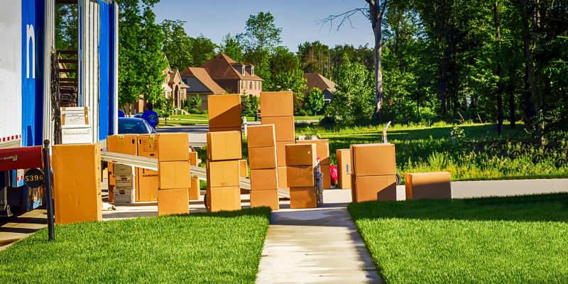 A few boxes in a yard, waiting to be moved into the house after a move. A nearly unloaded truck is parked nearby.